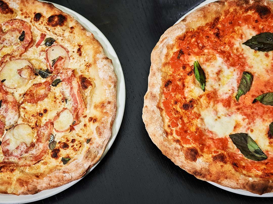 Two pizzas are sitting on plates on a table.