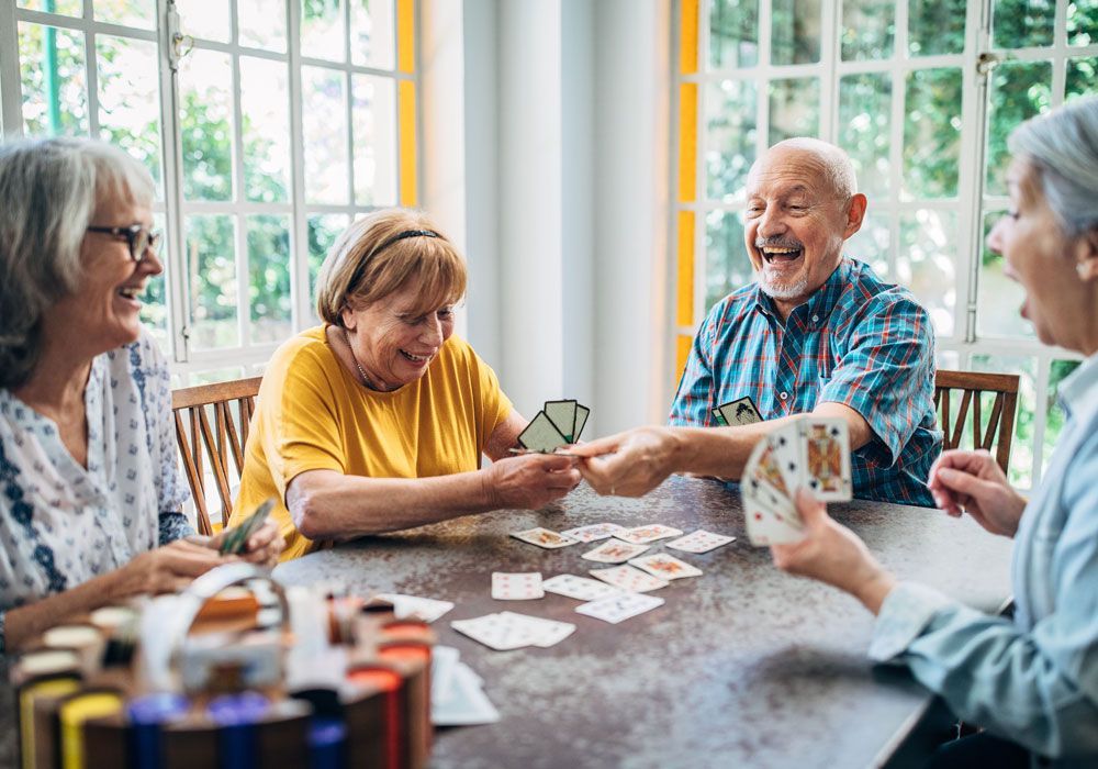 Friends playing cards at a bright table, smiling and laughing in a sunlit room