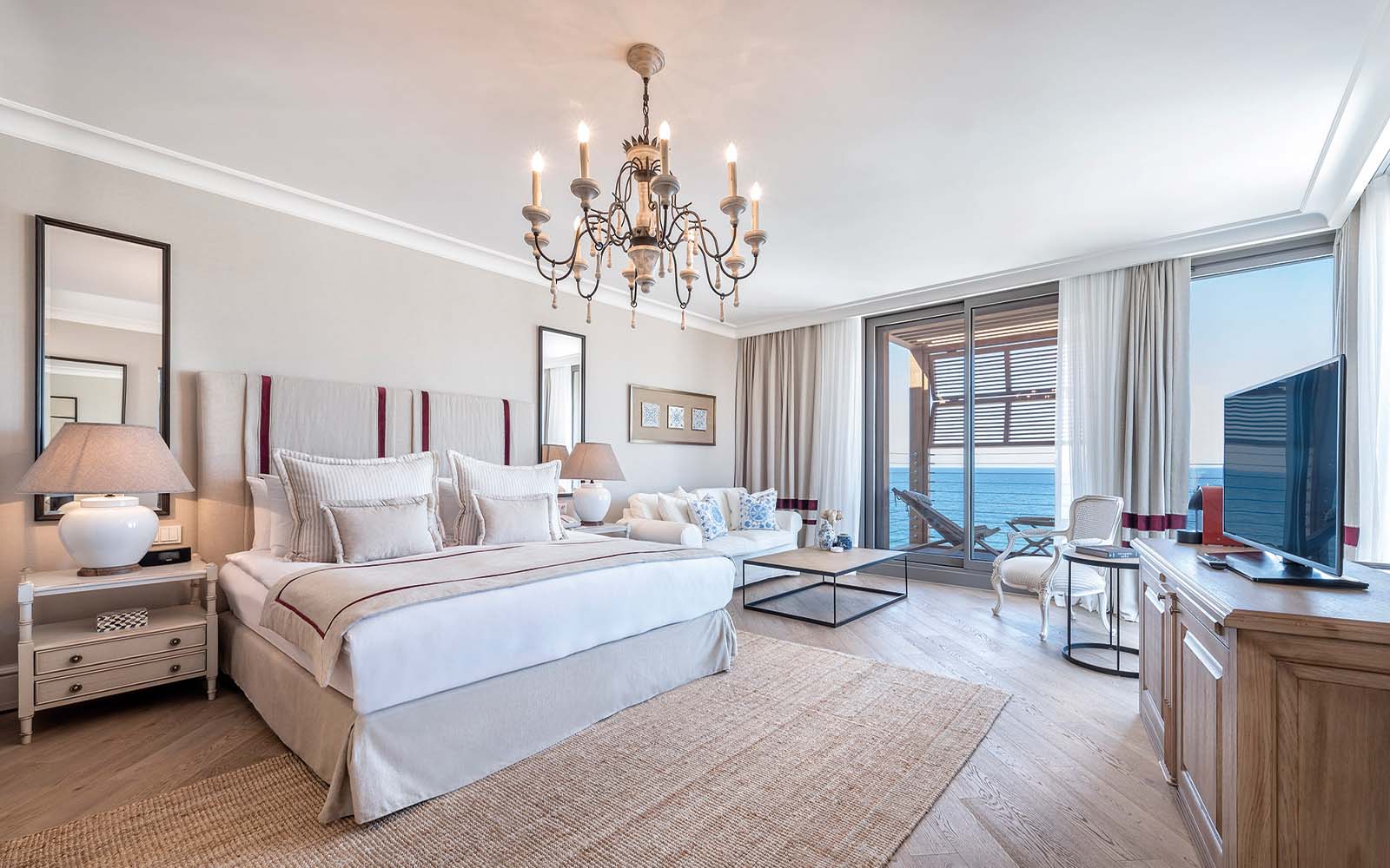 A bedroom with a king size bed , a chandelier , a couch , a television , and a large window