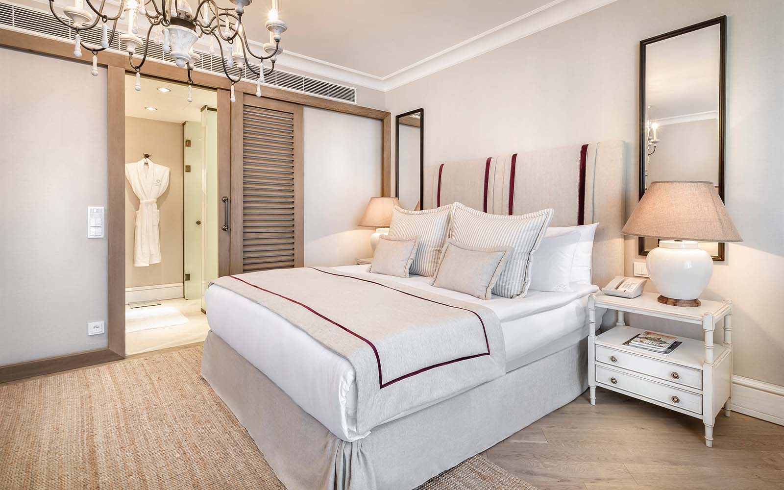 A bedroom with a bed , nightstand , lamp , mirror and sliding glass door leading to a bathroom.