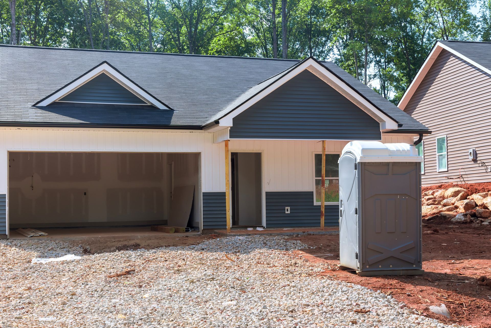 A house under construction with an open garage and portable toilet placed on a gravel driveway site A house under construction with an open garage and portable toilet placed on a gravel driveway site