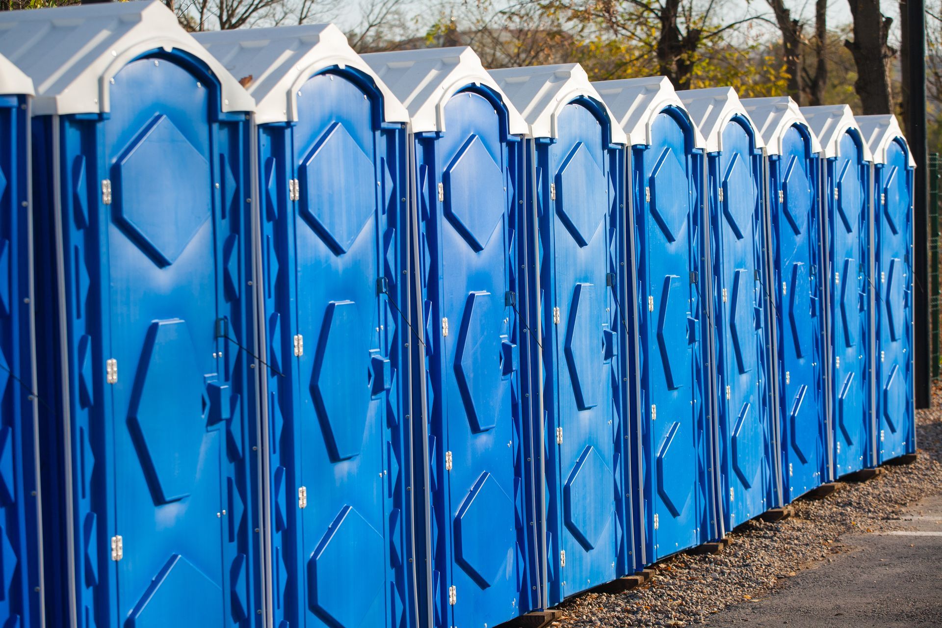 Row of blue portable toilets with white roofs lined up outdoors on gravel. Row of blue portable toilets with white roofs lined up outdoors on gravel.