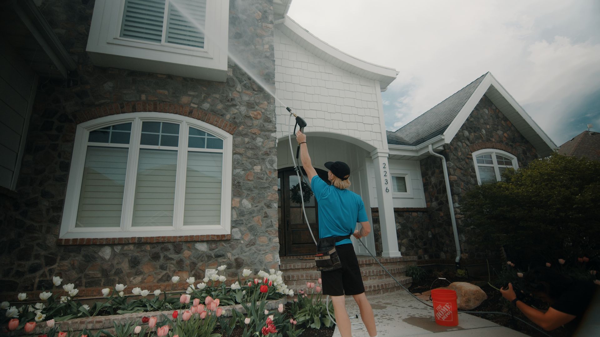 A man is cleaning the side of a house with a high pressure washer.