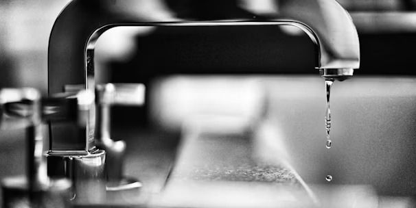 Black-and-white close-up of a faucet with a single droplet falling into a sink