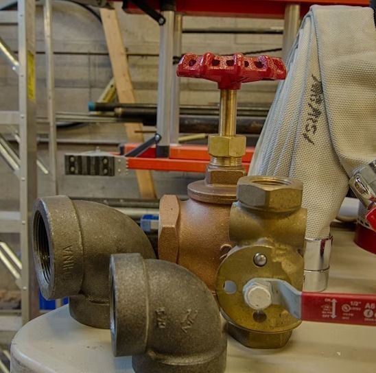 Industrial valve and pipe assembly with red handwheel on a workbench in a workshop