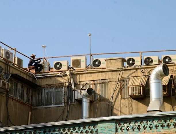 Rooftop with air conditioners, metal ducts, and tangled cables on a beige building under a clear blue sky