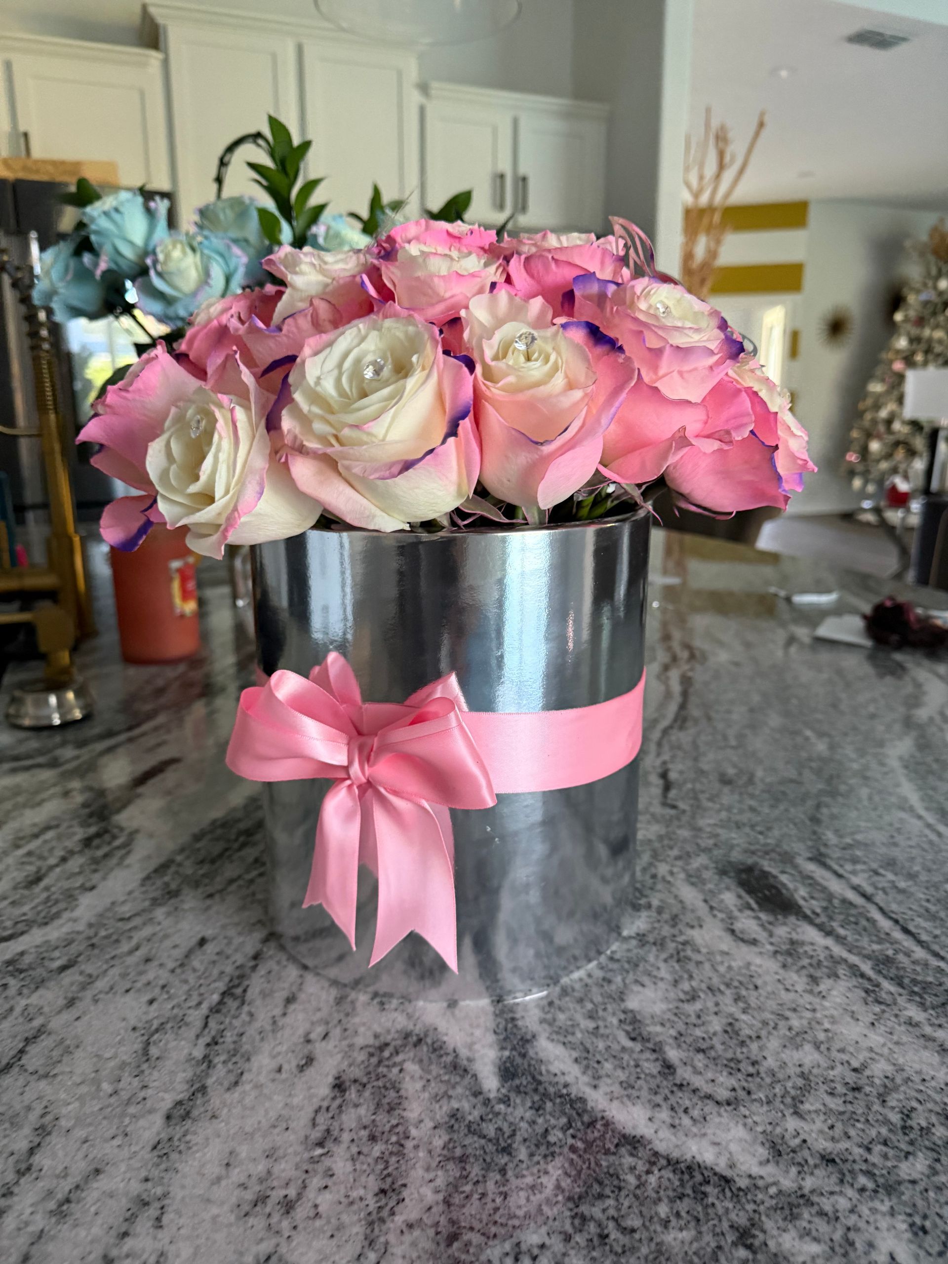 A silver vase filled with pink and white roses with a pink bow.