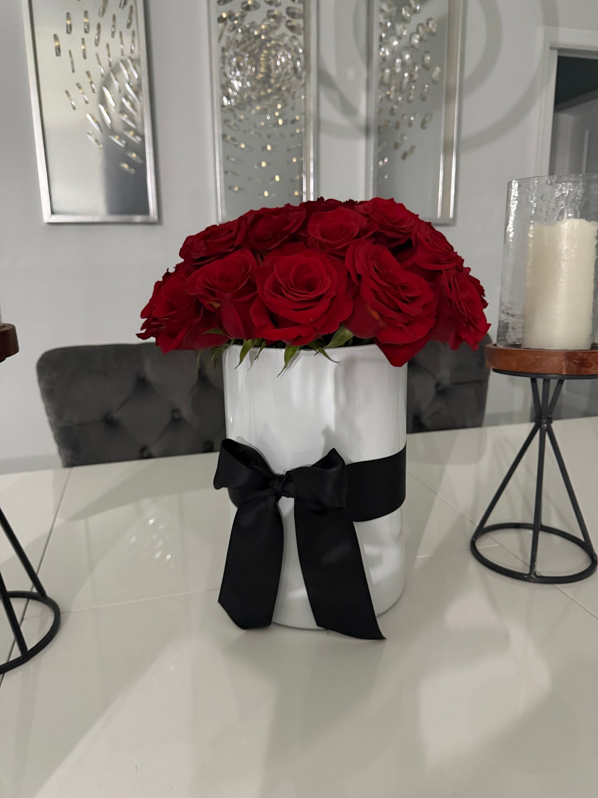 A white vase filled with red roses with a black bow