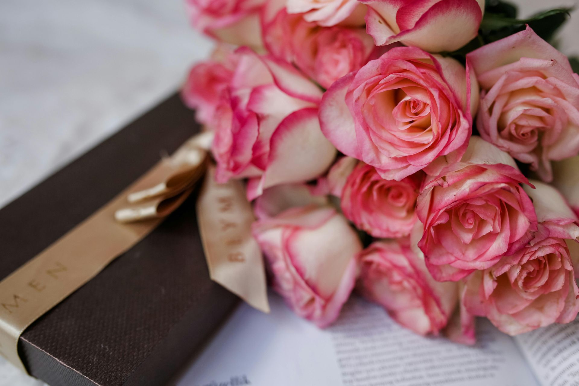 A bouquet of pink roses is sitting on top of an open book next to a gift box.