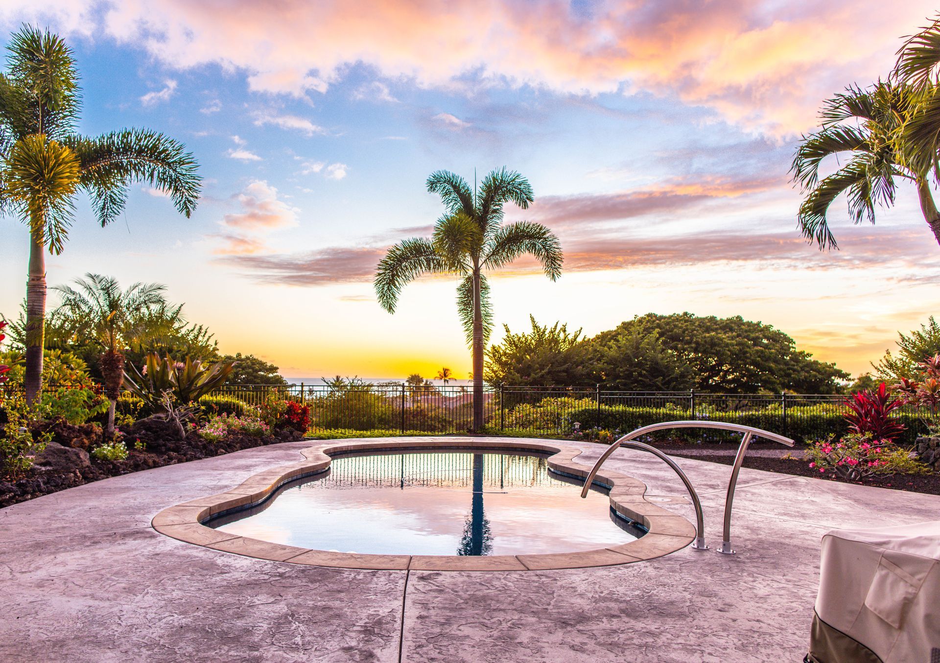 A large swimming pool surrounded by palm trees at sunset.