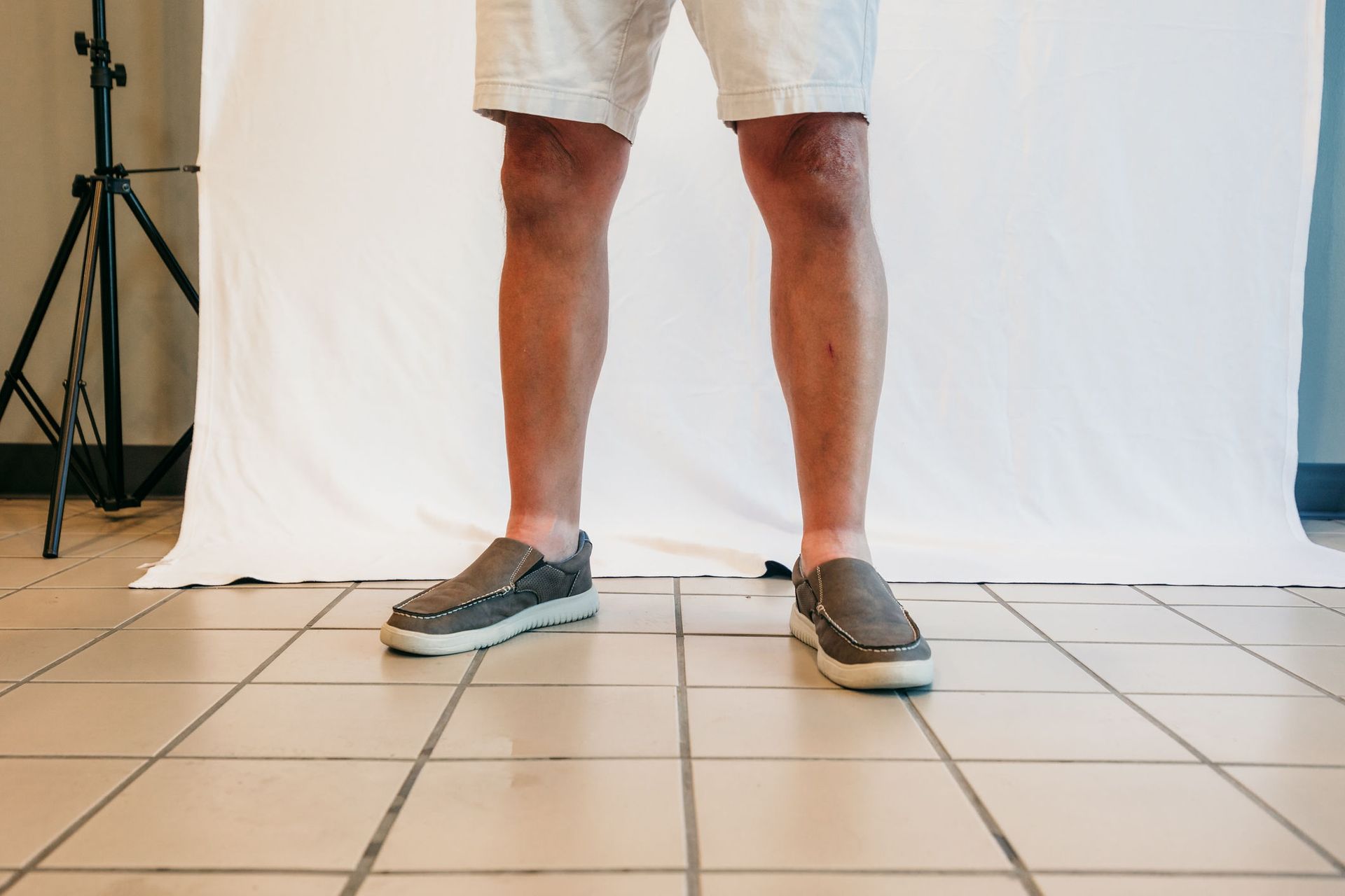 Lower legs in gray sneakers standing on tiled floor before a white backdrop