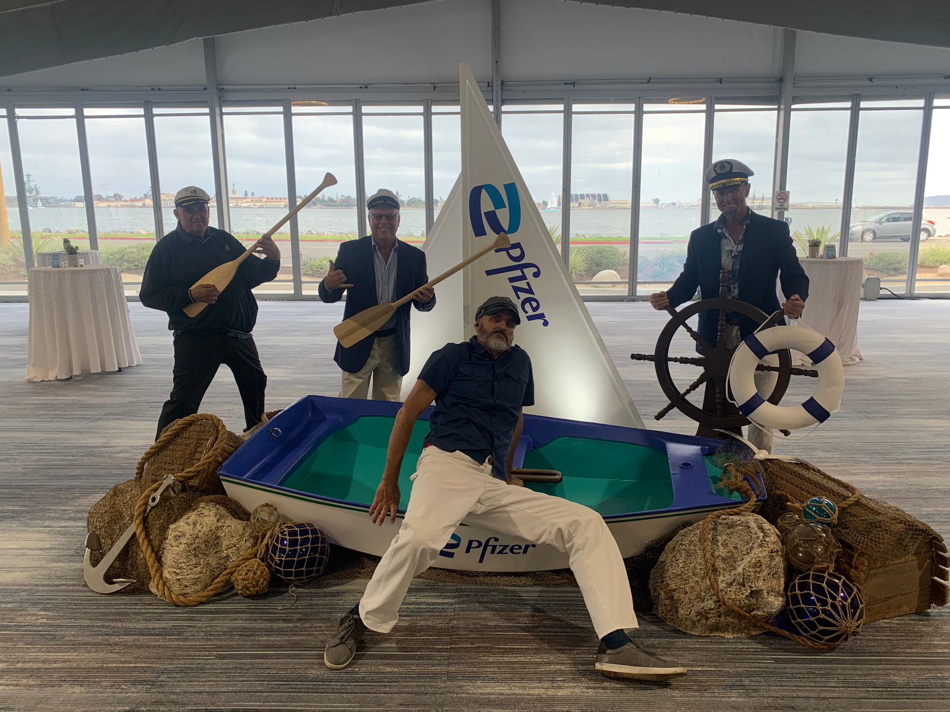 Four people posing with a small sailboat made of hay bales and a white sail indoors at a beachside pavilion