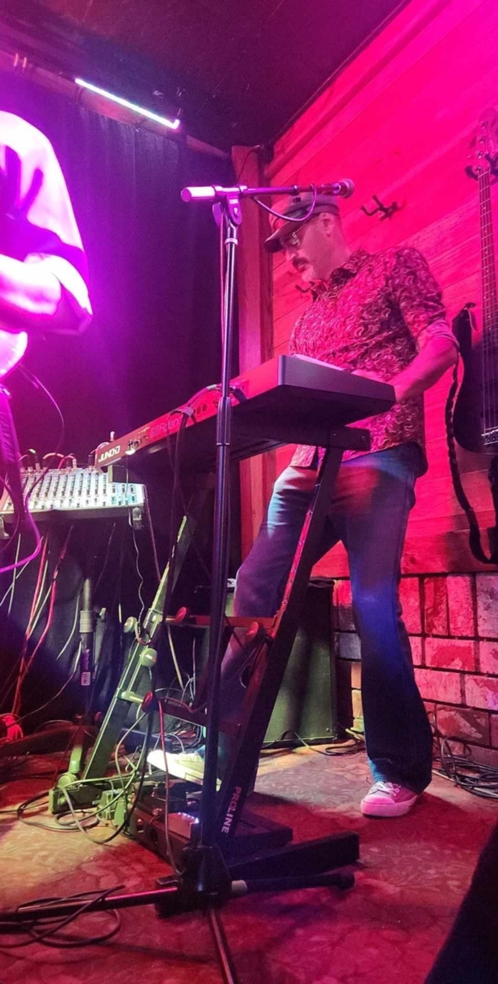 Person performing onstage with a keyboard and microphone under pink-purple lights