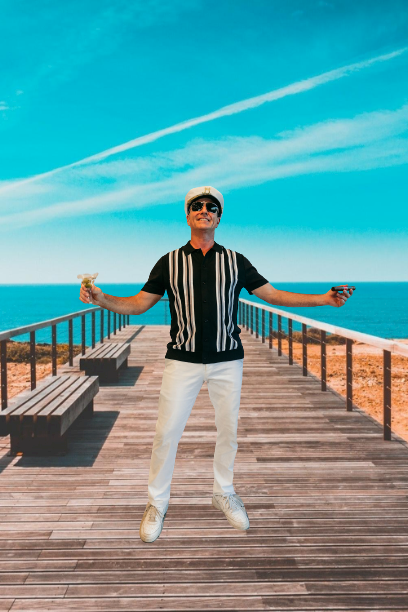 Person standing on a wooden pier with arms outstretched, ocean and blue sky behind.