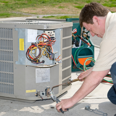 HVAC technician repairing an air conditioning unit outside, using a torch.