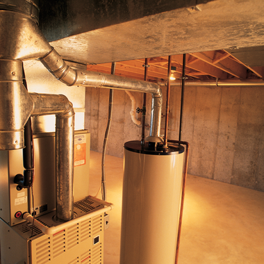 Furnace and water heater in a basement with ductwork and exposed ceiling.