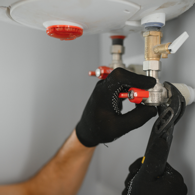 A person in black gloves using a wrench to adjust plumbing valves on a water heater.