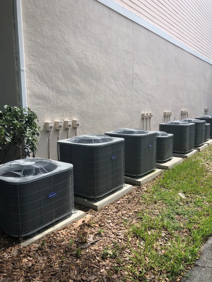Row of AC units against a building with electrical boxes along the wall.