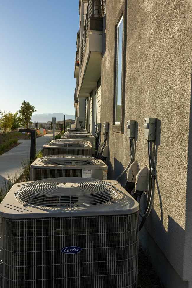 Row of air conditioning units against a building with a walkway on a sunny day.