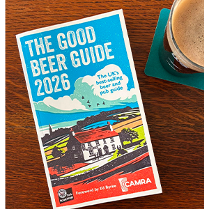 Blue book titled “The Good Beer Guide” next to a glass on a wooden table.
