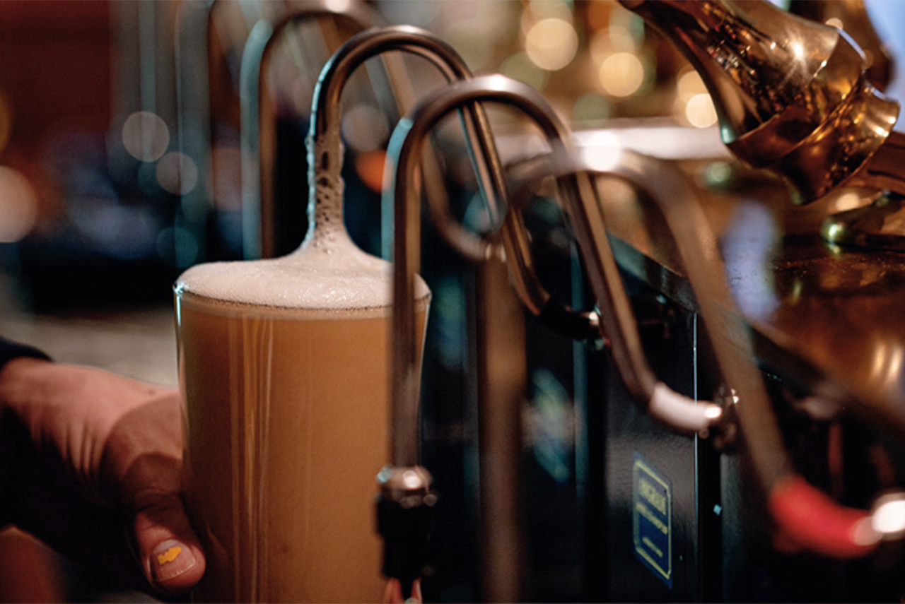 Hands pouring a foamy beer from a tap in a bar close-up