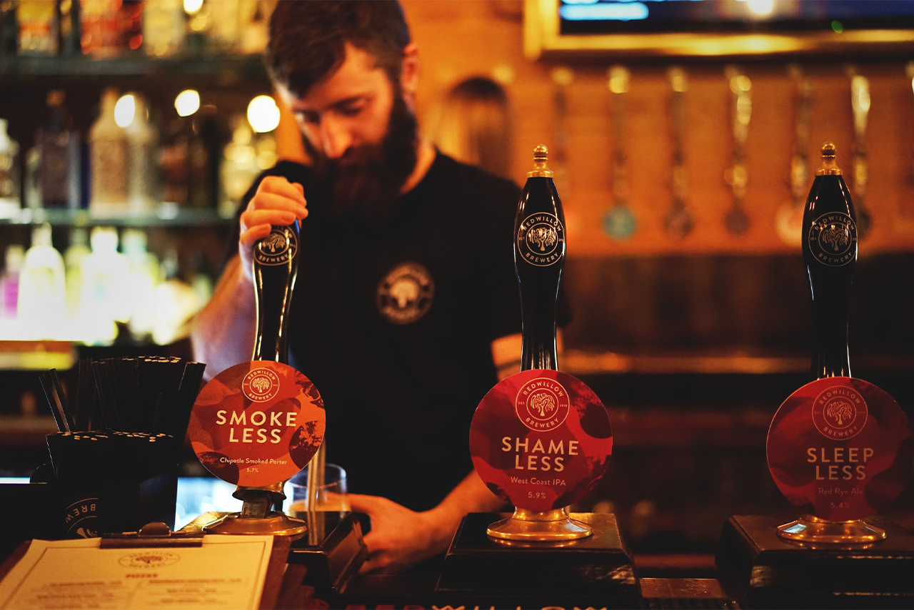 Bartender pouring beer in a warm-lit bar with three branded taps on the counter