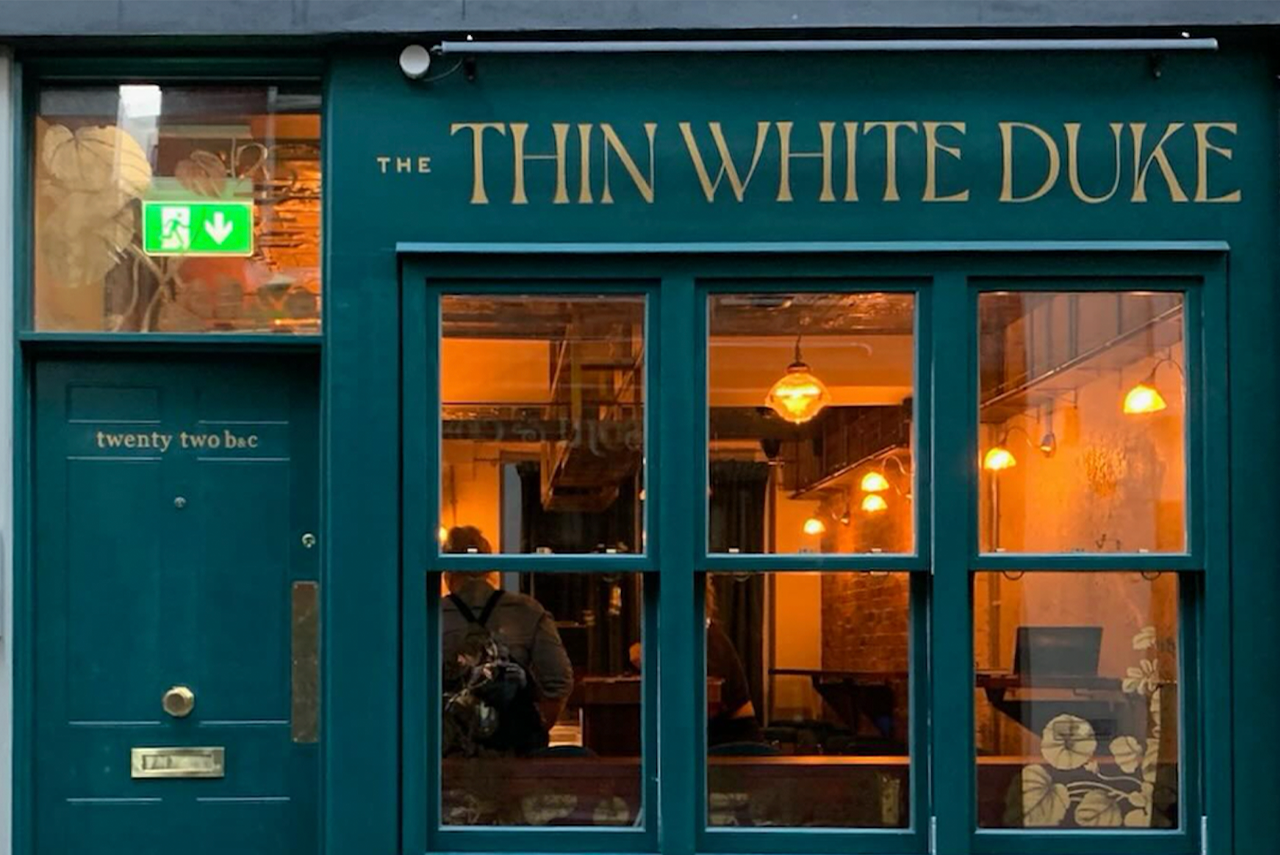 Teal storefront of The Thin White Duke pub with lit windows and wooden door