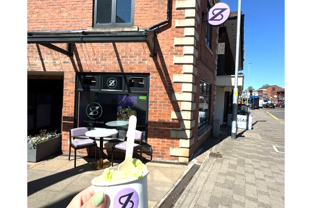 Street view of a brick café with outdoor tables and a purple sign on a sunny day