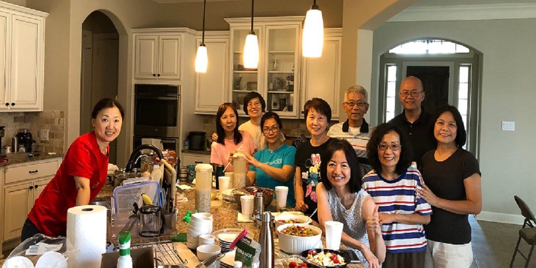 A group of people standing together in a kitchen around a large island, smiling at the camera.