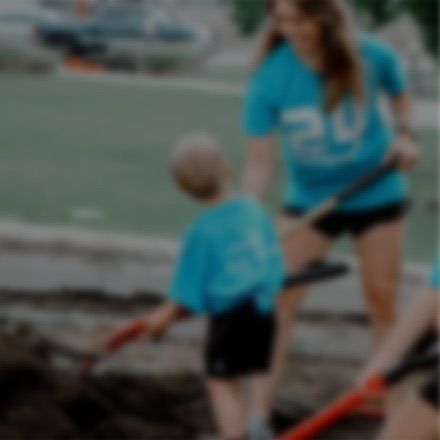 People wearing matching blue shirts shovel dirt in an outdoor area.