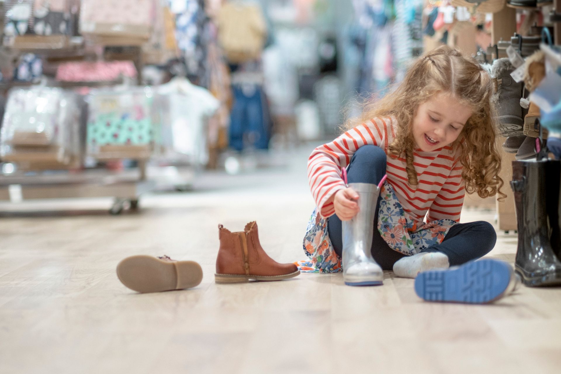 Una bambina è seduta sul pavimento e sta provando un paio di stivali da pioggia.