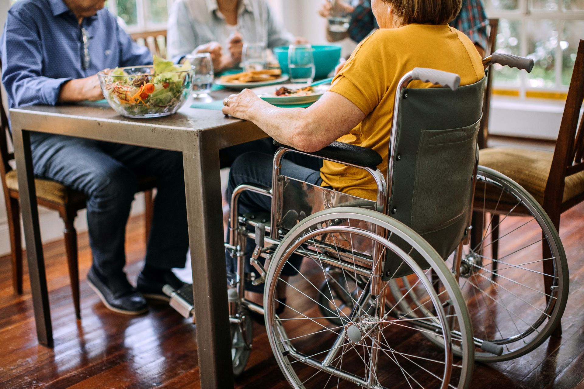 Una persona in sedia a rotelle pranza con altre persone a un tavolo di un ristorante.