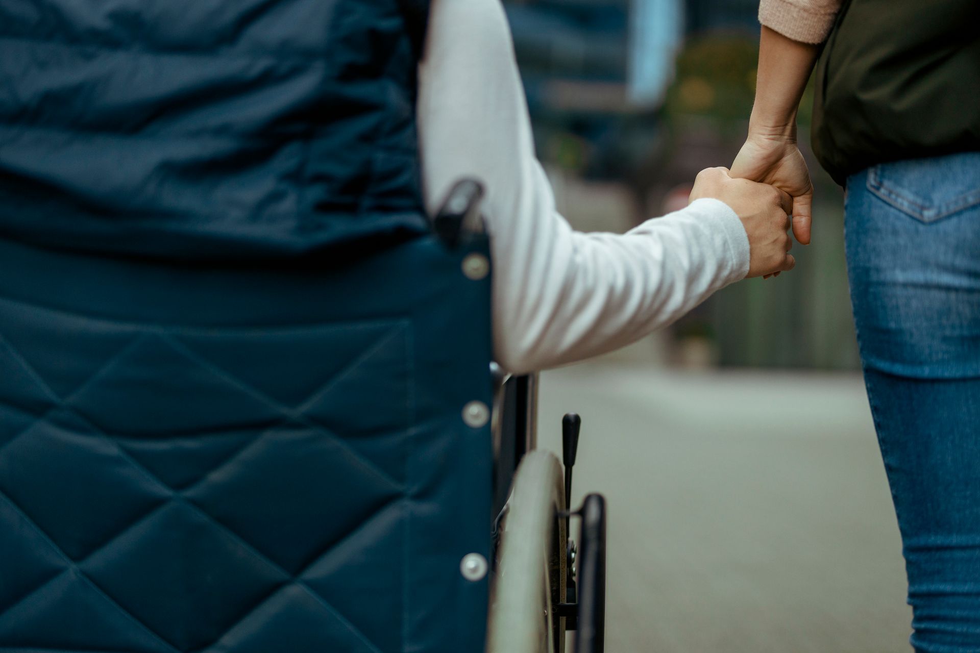 Due persone che si tengono per mano vicino a una sedia a rotelle in un ambiente esterno.