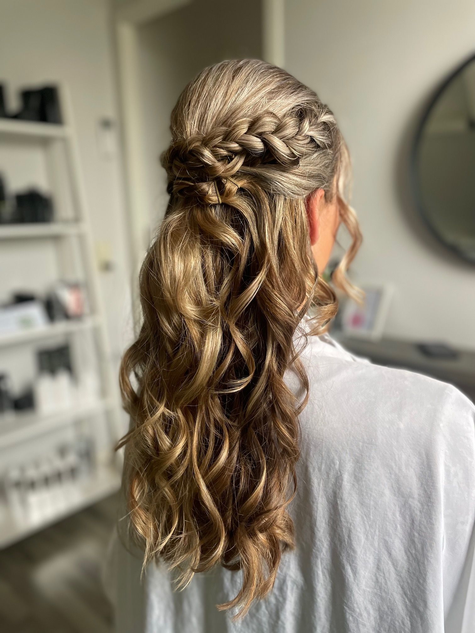 Vrouw met golvend blond haar, half opgestoken met een vlecht bovenop, draagt een witte blouse.