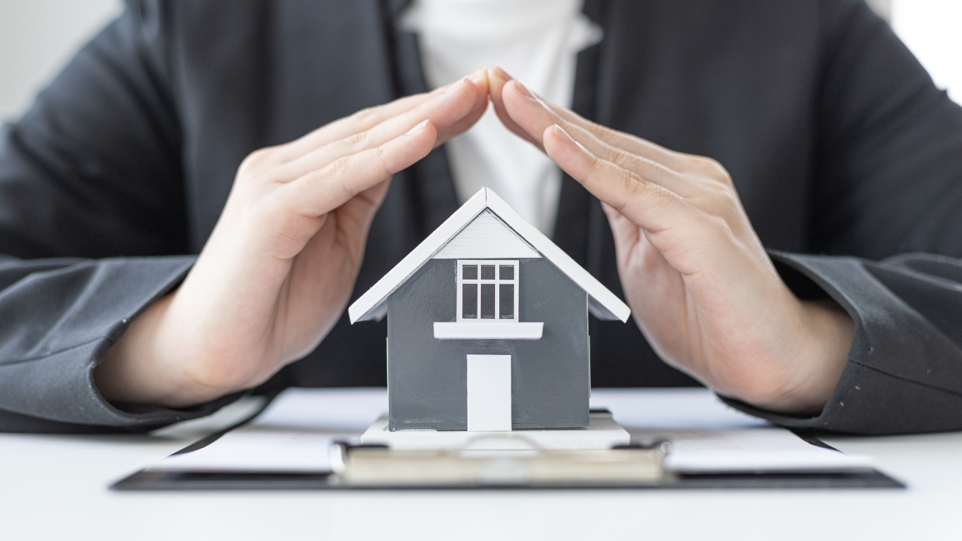 Hands cupped over a miniature gray house, symbolizing protection.