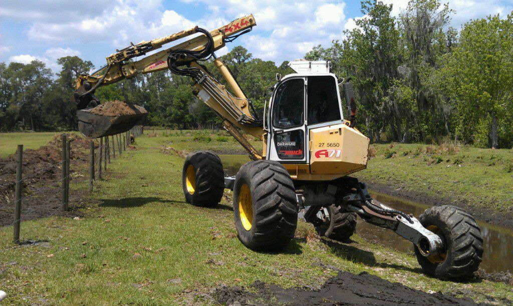 A yellow excavator is digging a hole in a grassy field