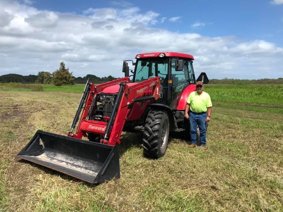 A man is standing in front of a red tractor in a field.