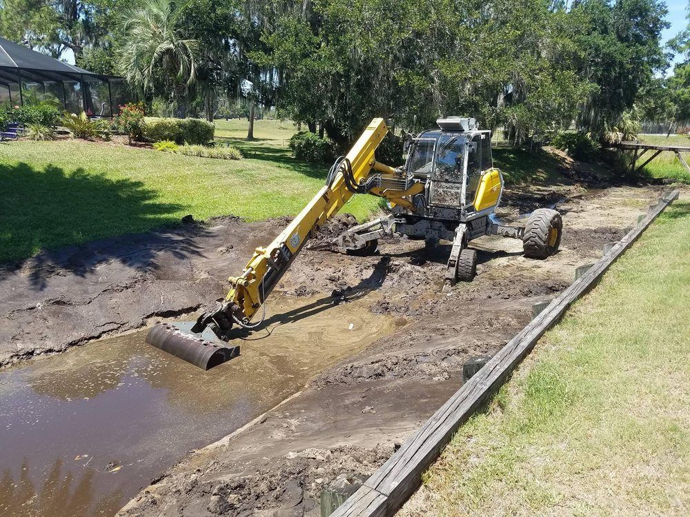 A yellow excavator is digging a stream in a yard.