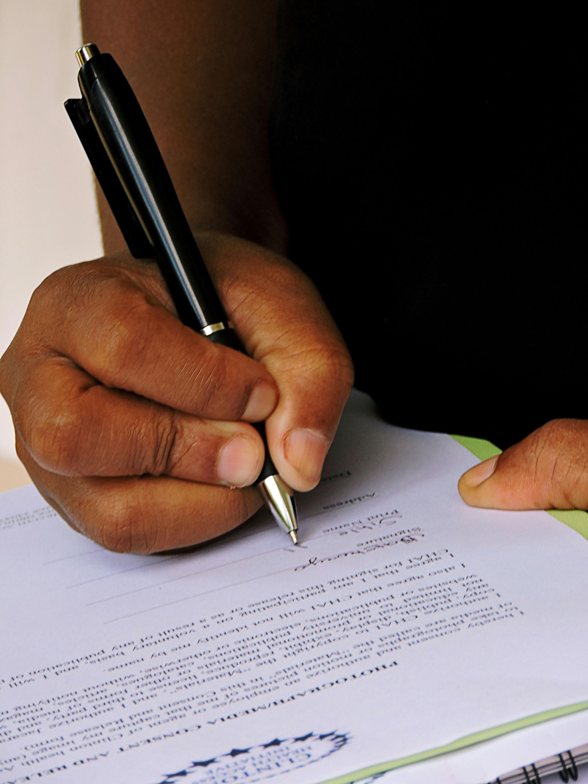 Hand holding a black pen and signing a document on a white page