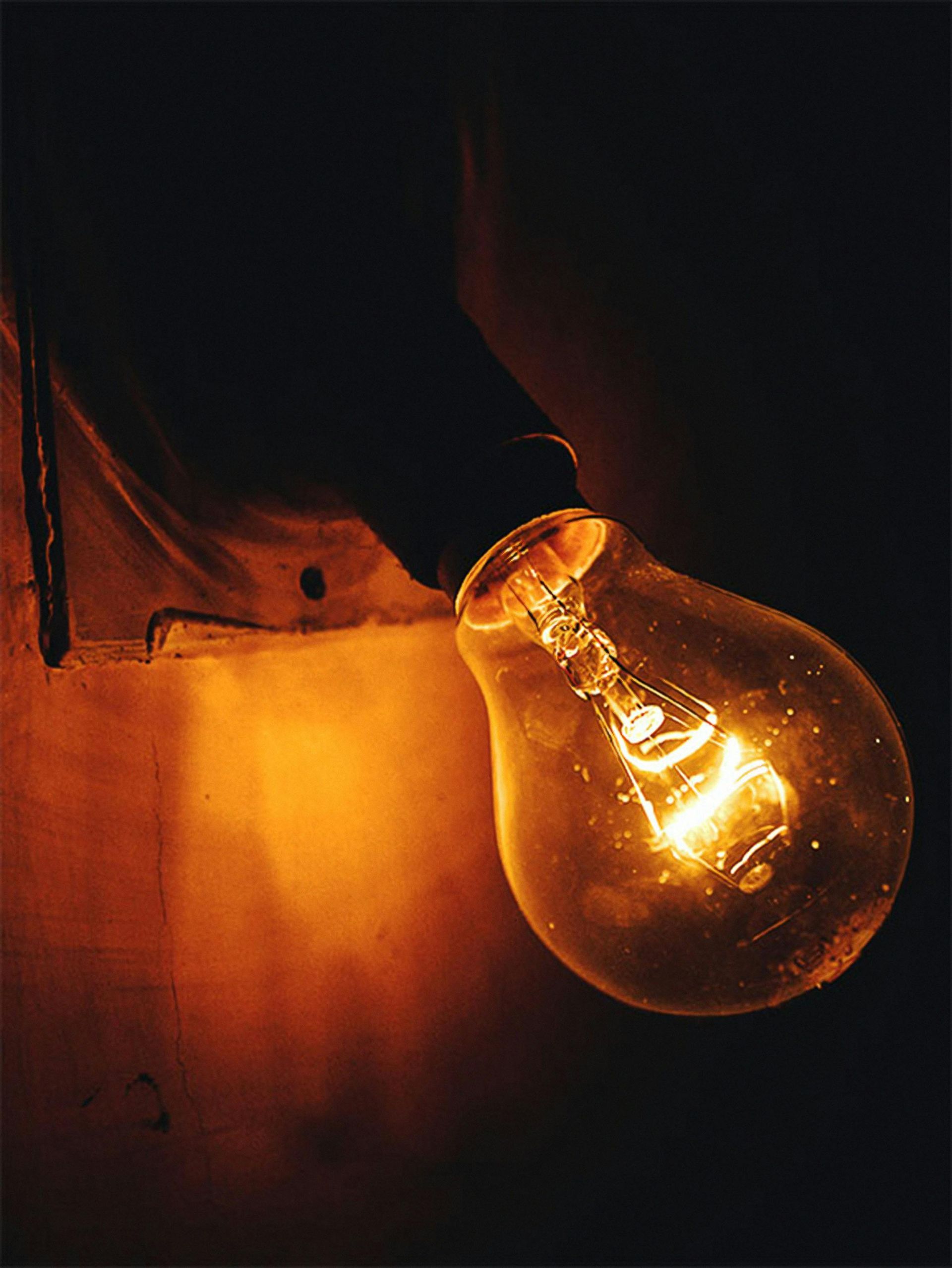 Glowing incandescent light bulb hanging against a dark, warm-toned background