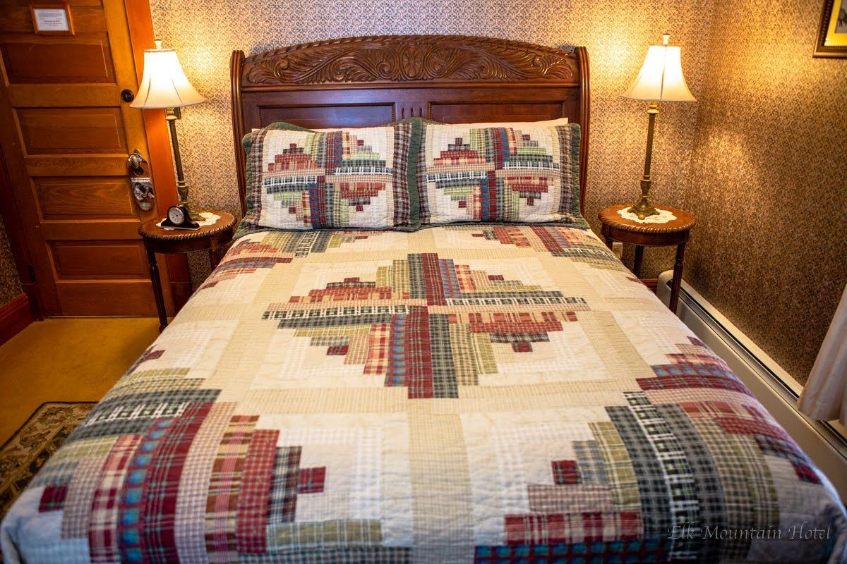 A bed with a quilt and pillows in a room with two lamps.