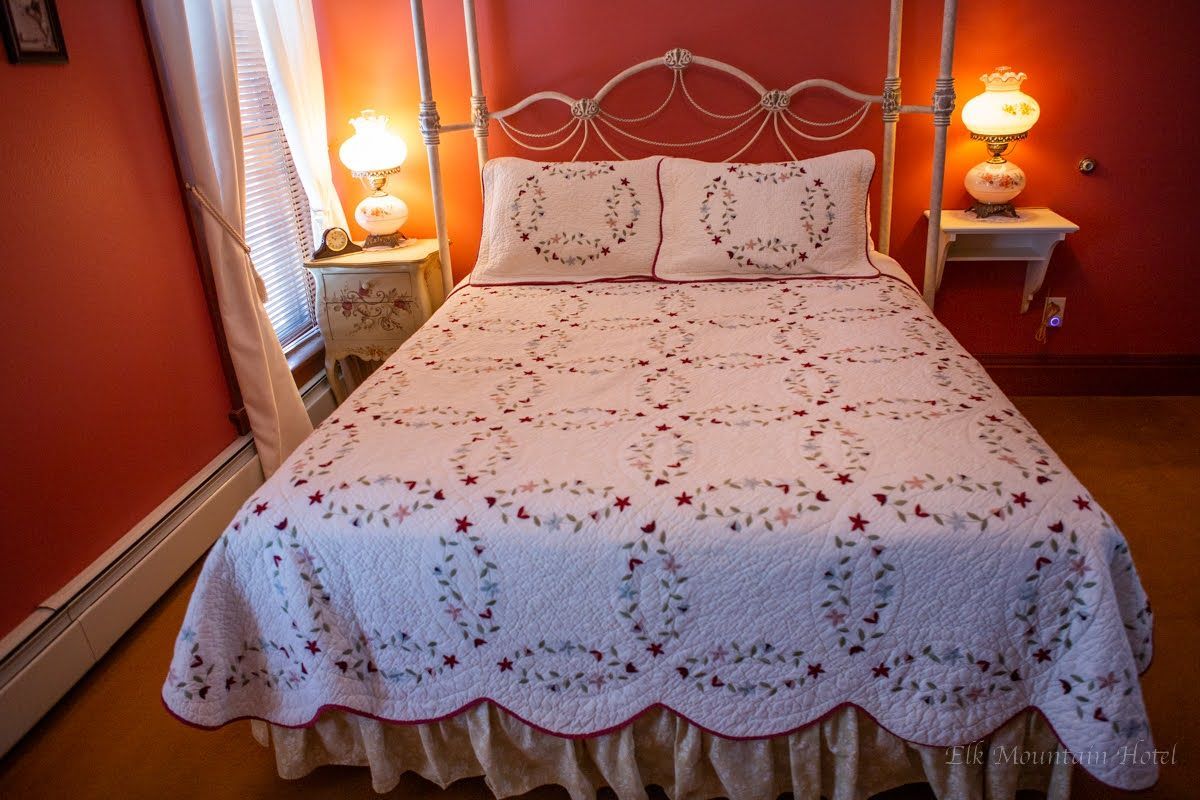 A bed with a quilt on it is in a bedroom with red walls.