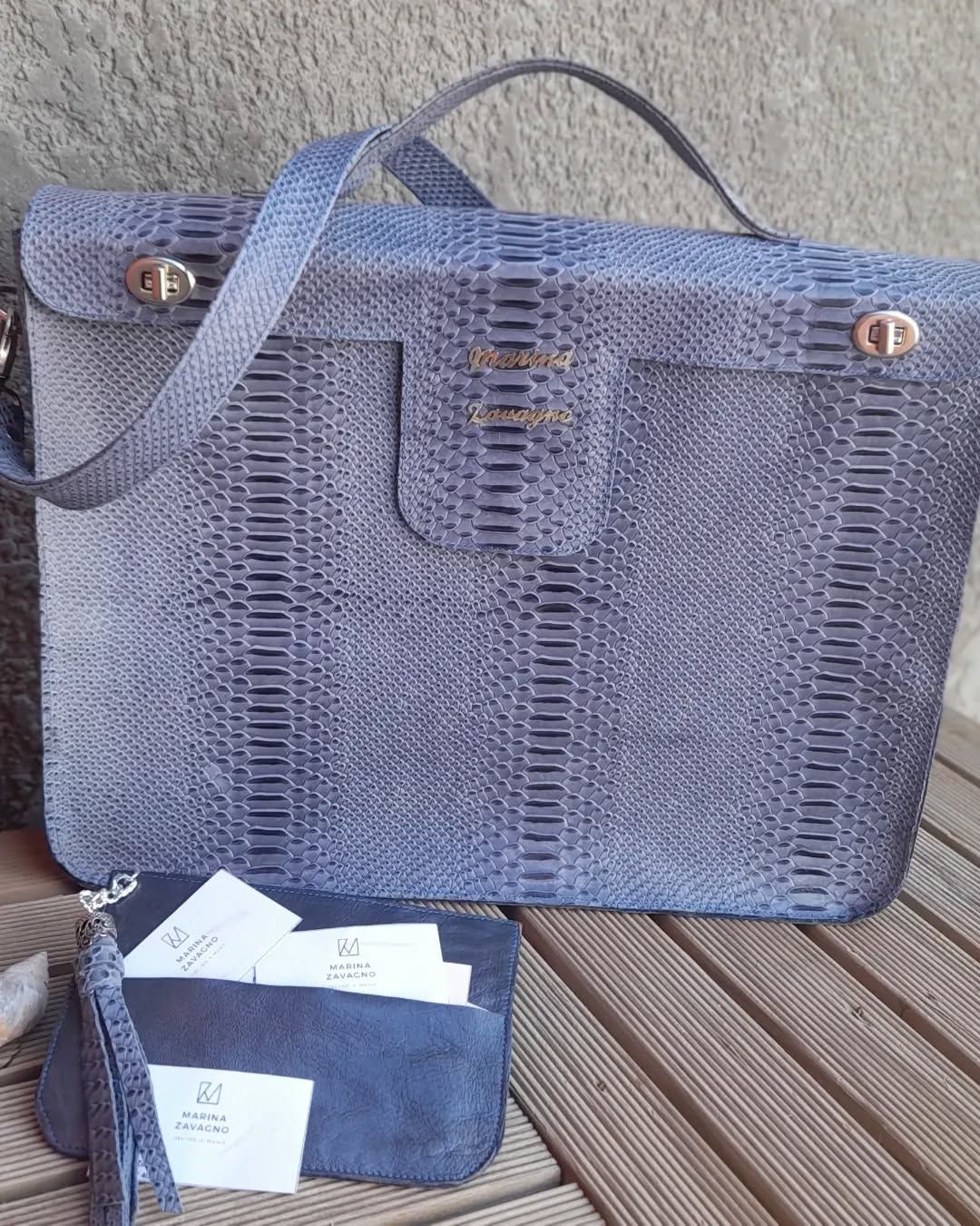 Bolso de mano con textura de piel de serpiente de color azul y clutch a juego sobre superficie de madera.