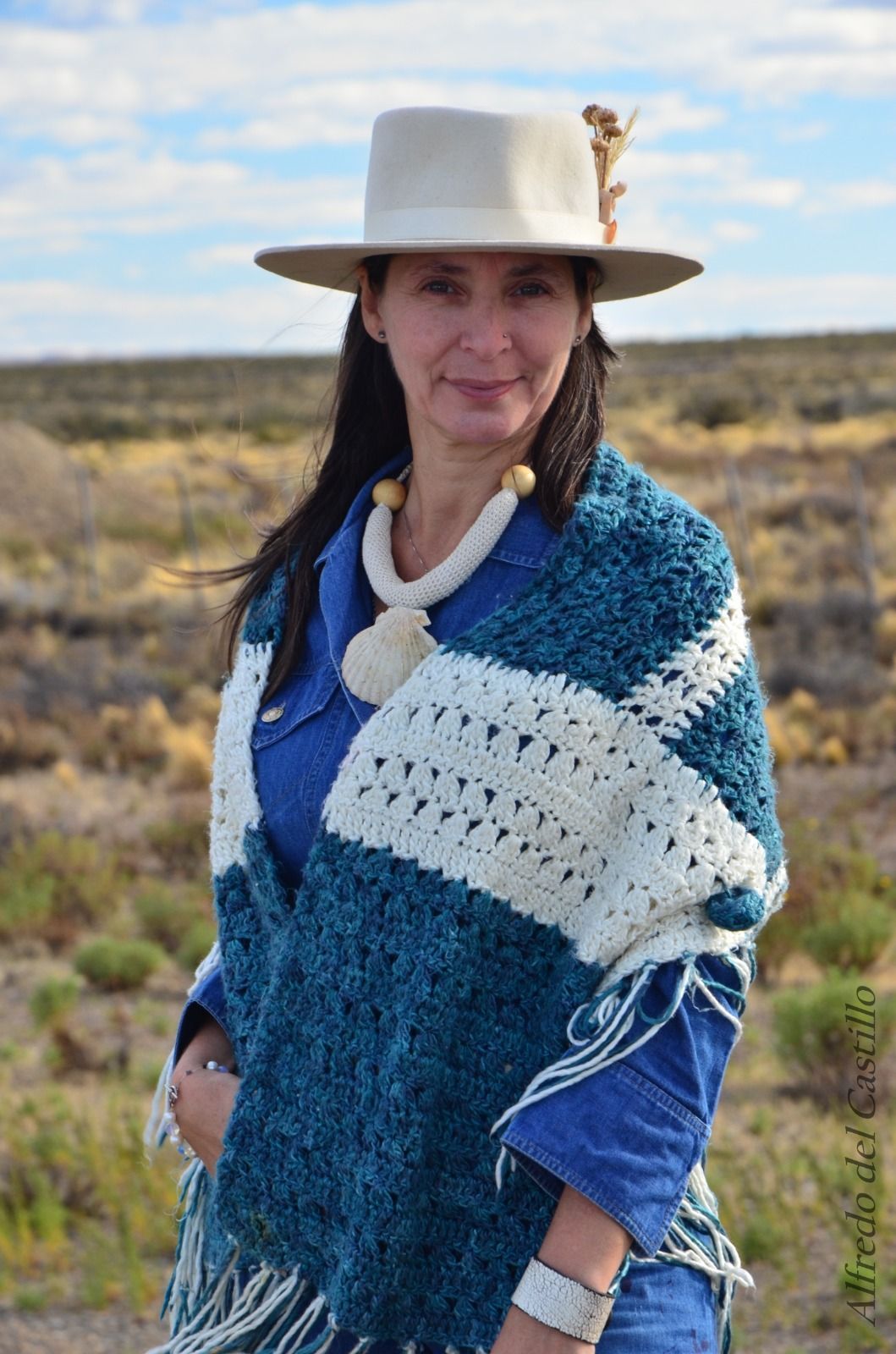 Mujer con poncho azul y sombrero, sonriendo al aire libre.