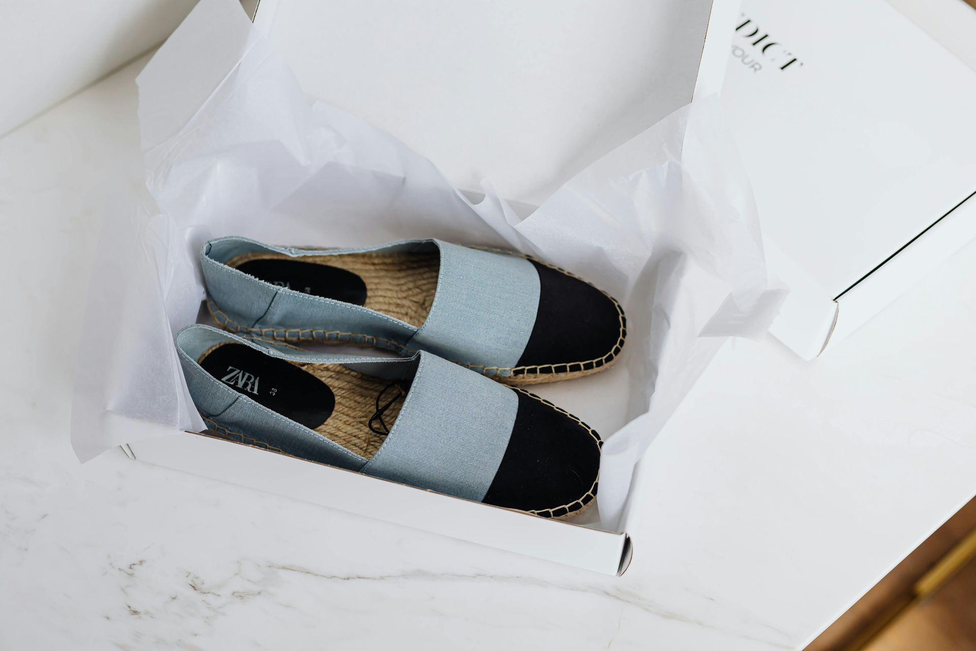 Zapatos azules sin cordones en una caja de zapatos blanca, envueltos en papel de seda.