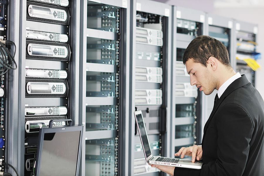 A man in a suit is using a laptop in a server room