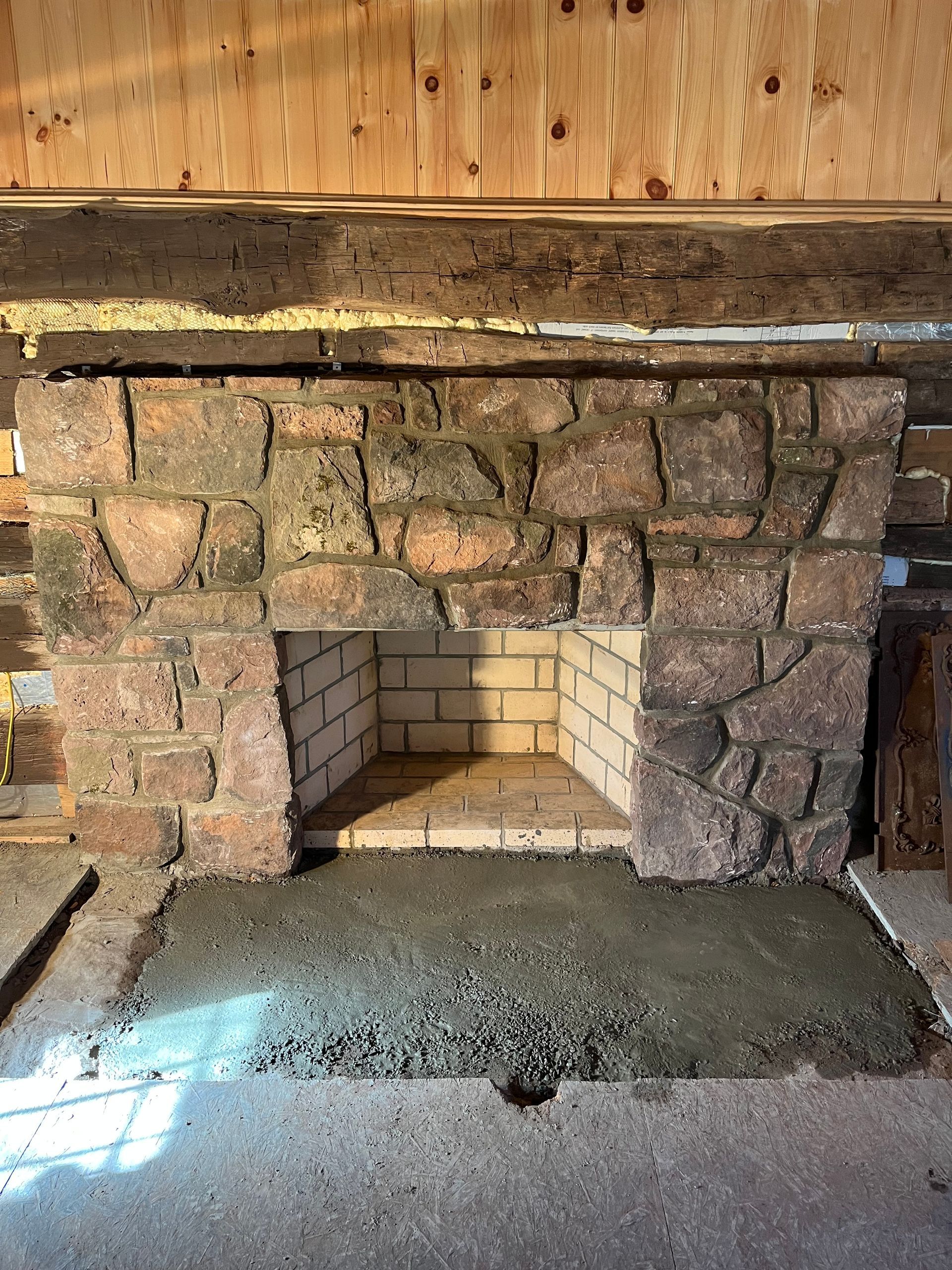 Stone fireplace with new concrete hearth, inside a wood-paneled cabin.