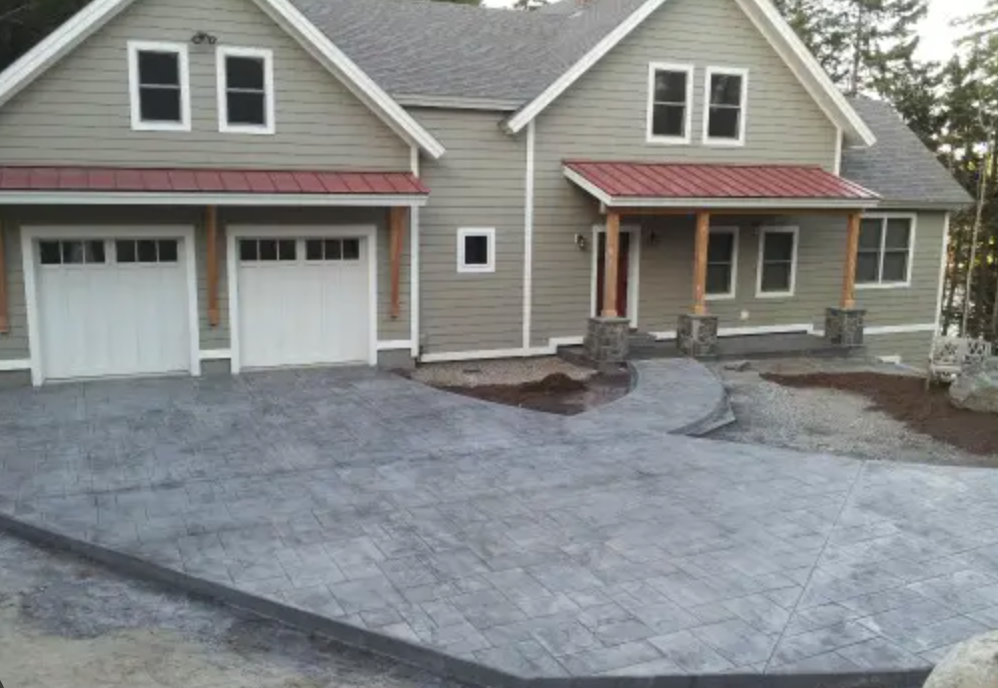 House with stamped concrete driveway; gray siding, red roof accents, two-car garage, and front porch.