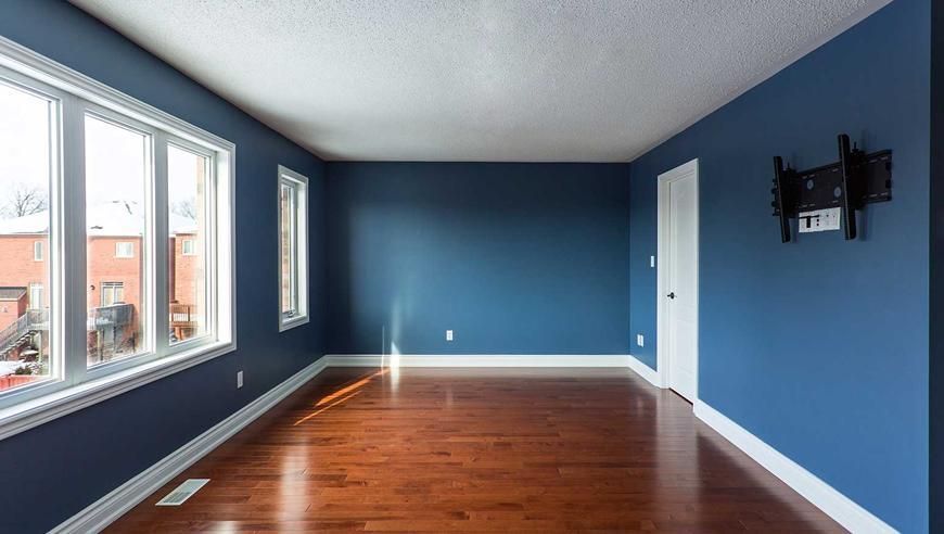 Empty room with blue walls, white trim, wood floor, windows, and TV mount.