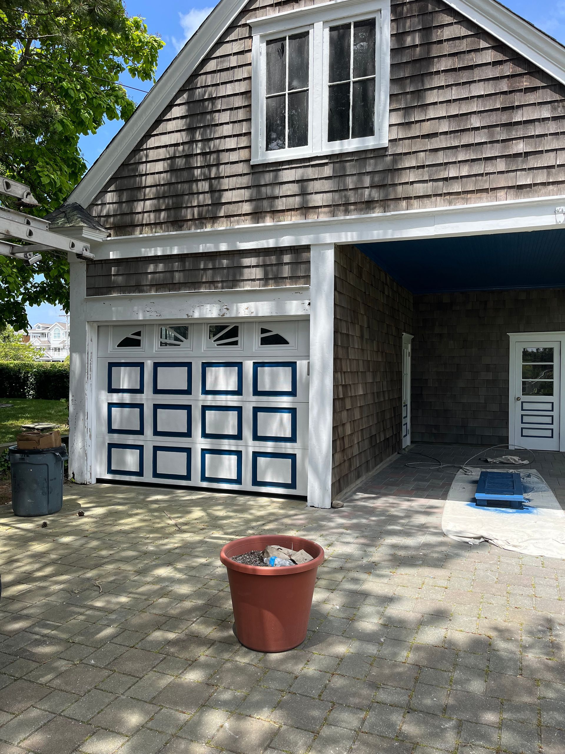 Garage with blue and white door, cedar shingles, and a brick patio.